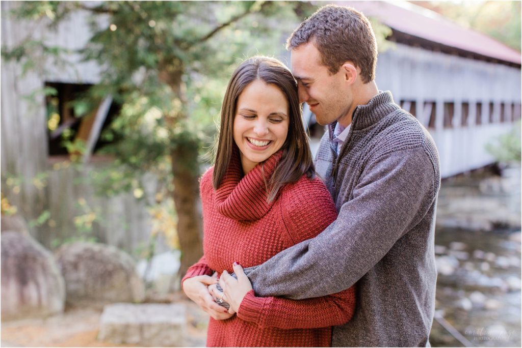 couple standing in front of covered bridge at sunset