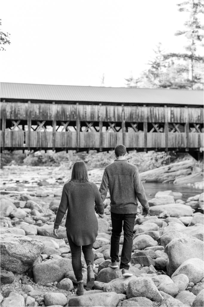 couple walking on river rocks by covered bridge