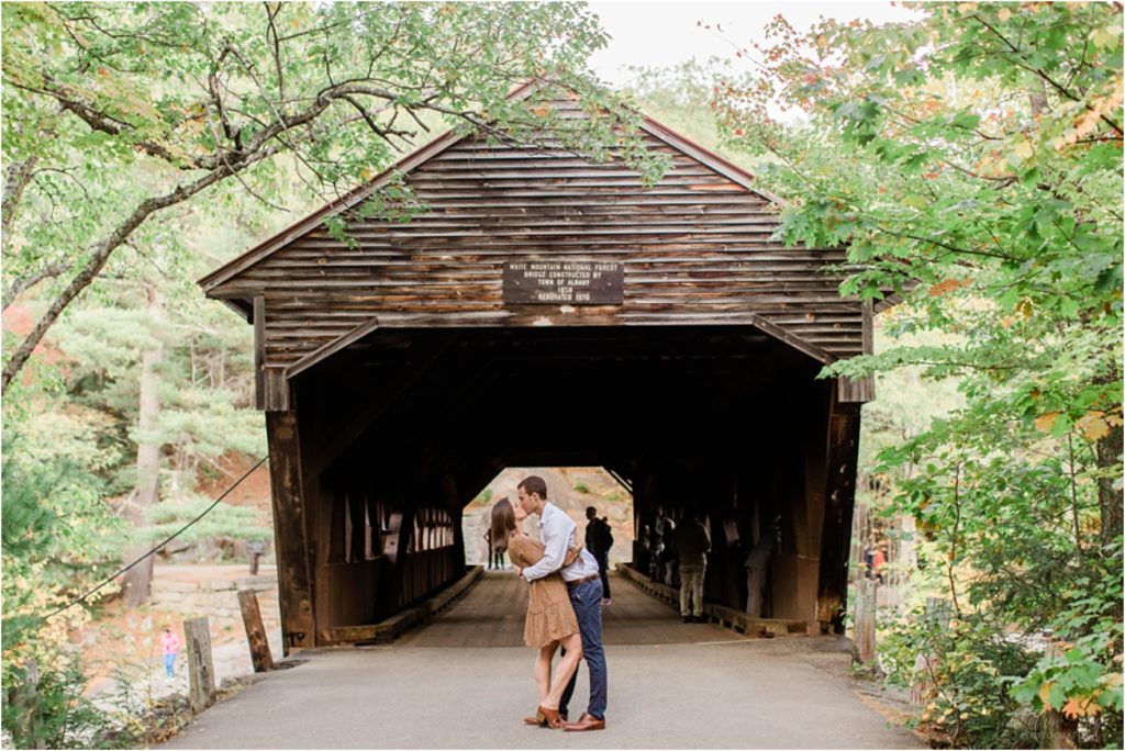 man and woman kissing in front of covered bridge