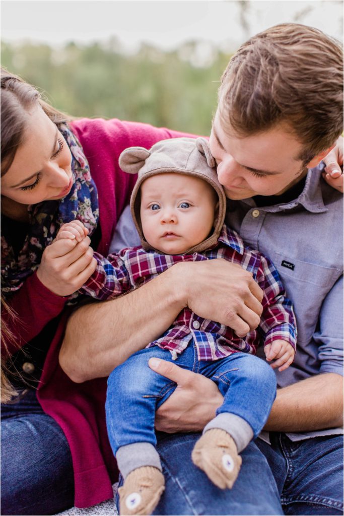 Baby in bear hat being kissed by his parents