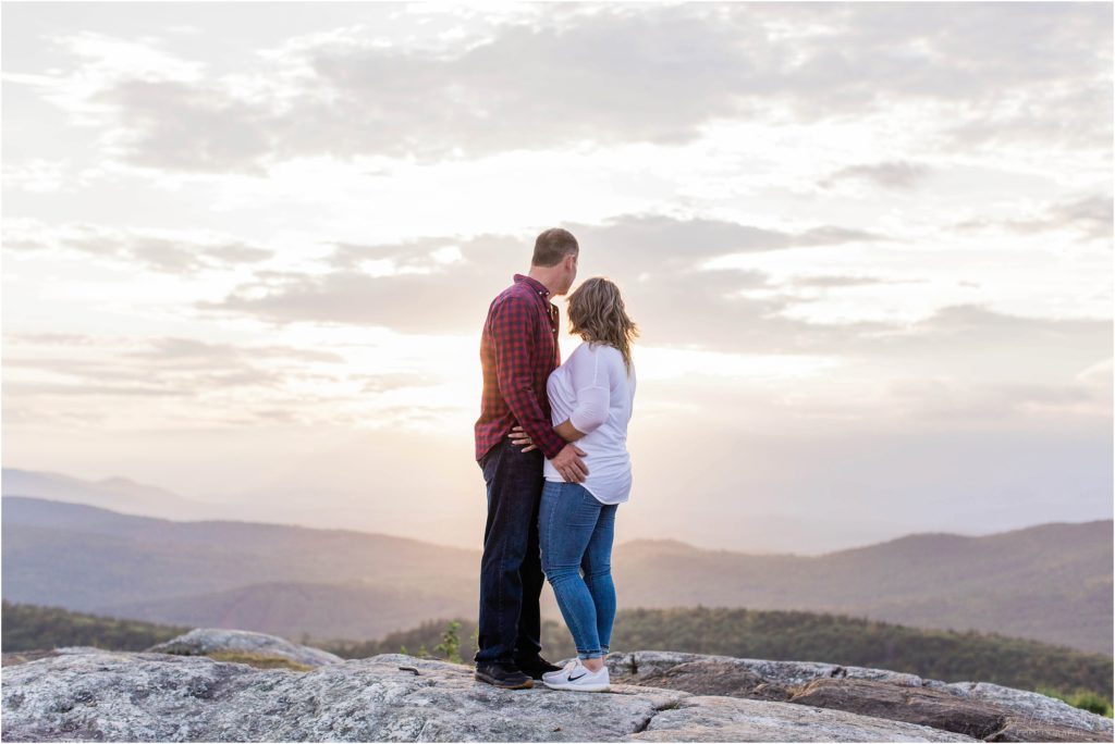 man and woman standing together on mountain top at sunset