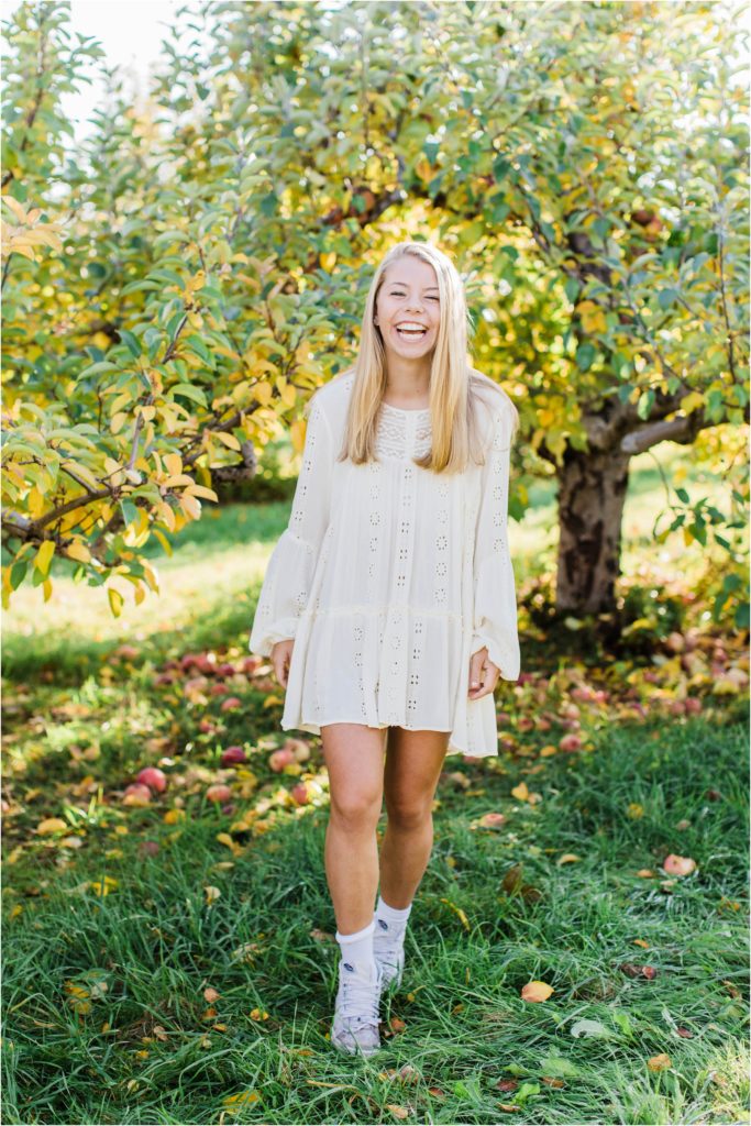 Senior girl dancing around in apple orchard in white dress