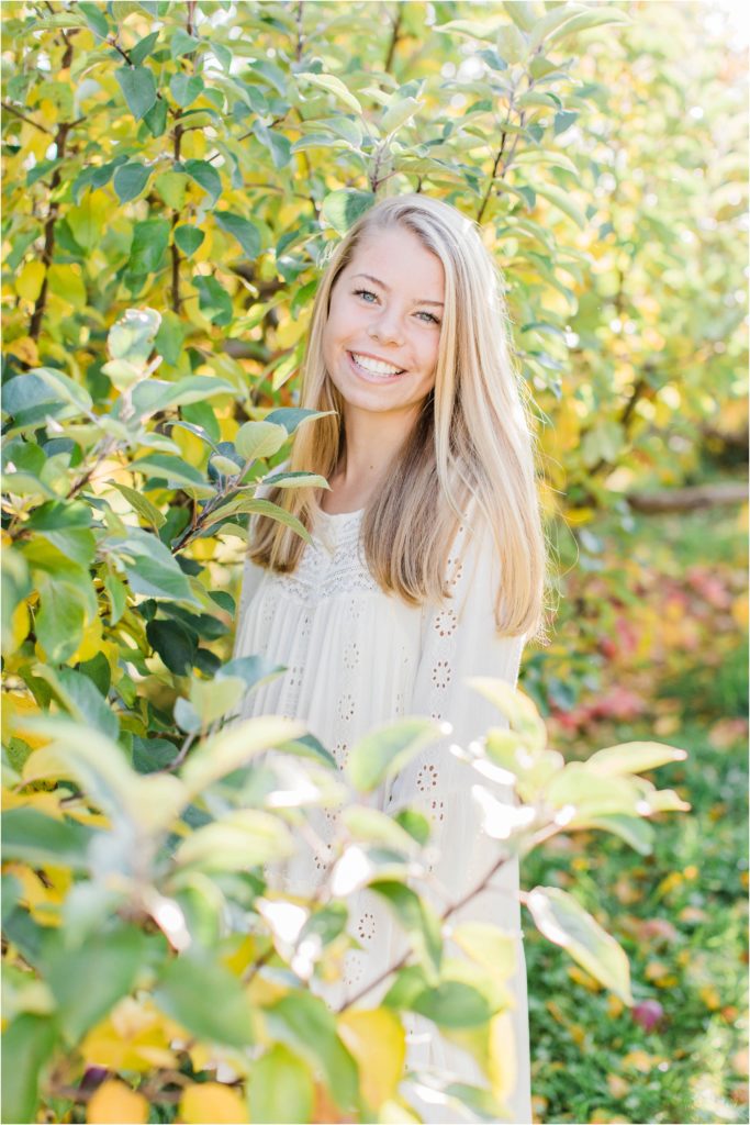 Senior girl standing in apple trees in white dress