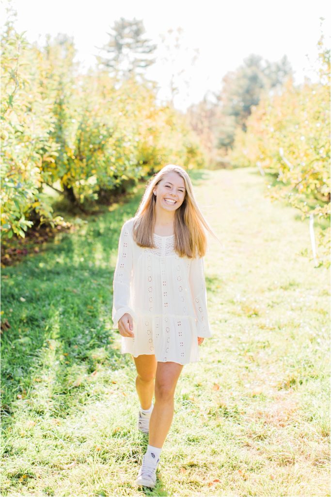 Senior girl walking in apple orchard in white dress