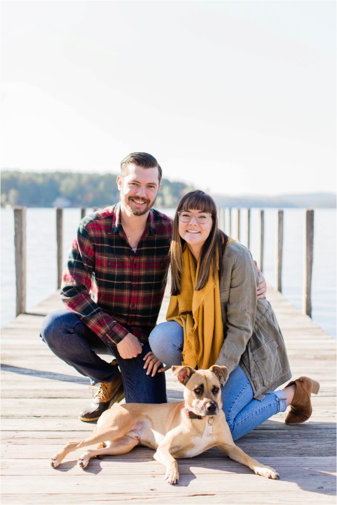 couple sitting together with dog on dock fall engagement photos