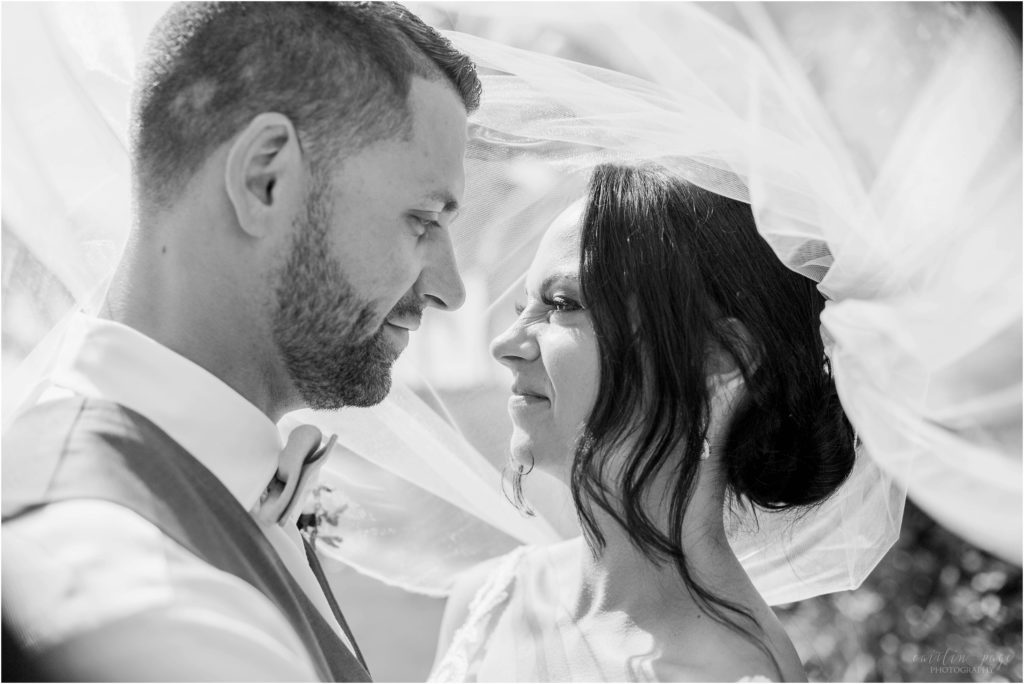 black and white portrait of bride and groom standing together under wedding veil