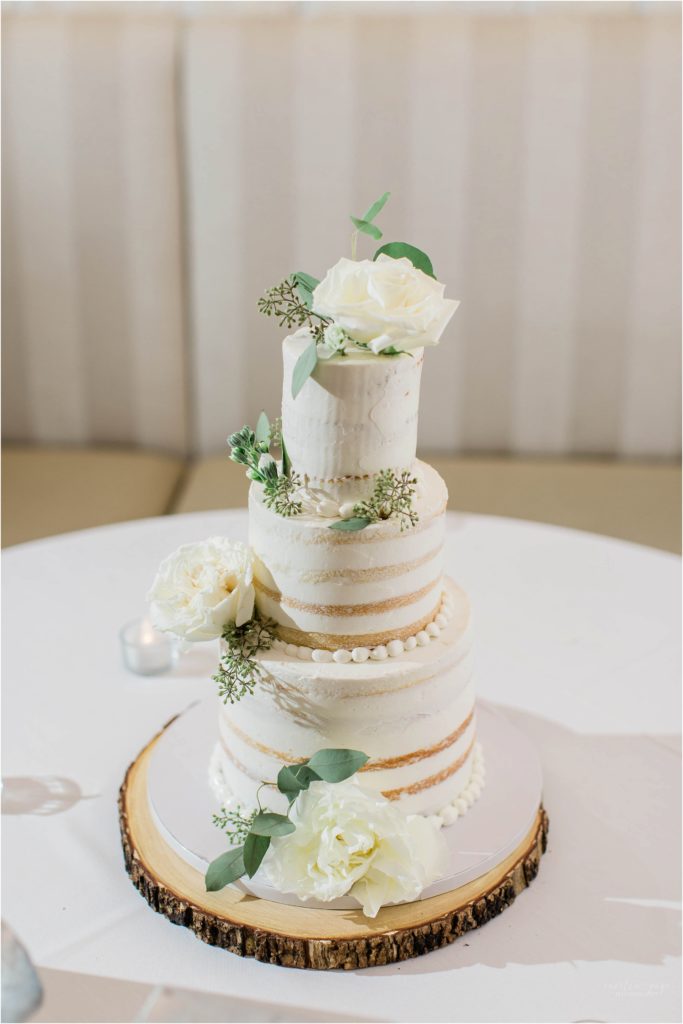 three tiered white naked cake with greenery and white flowers