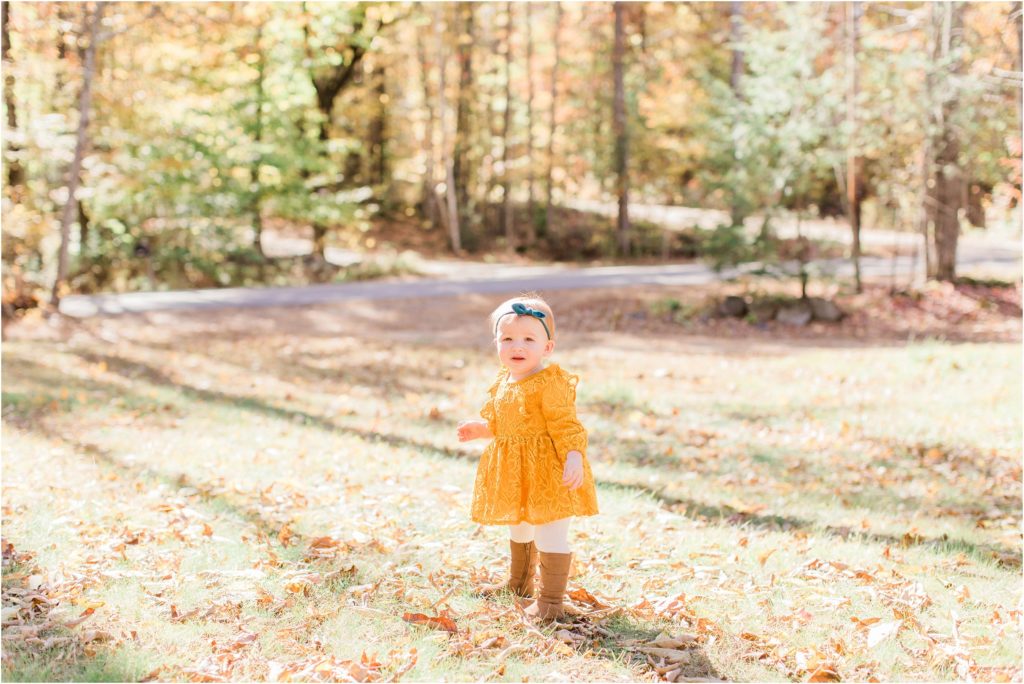 toddler in mustard colored dress standing in yard with leaves