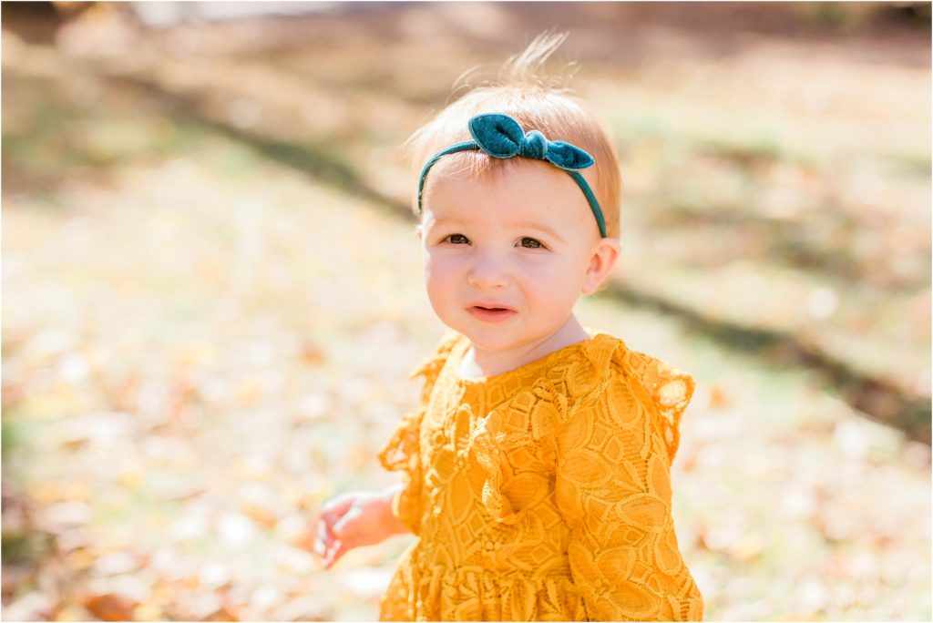 toddler in mustard colored dress standing in yard with leaves