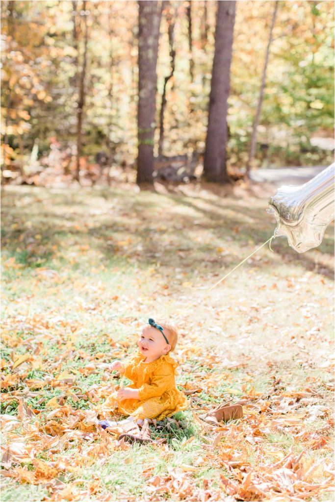 toddler in mustard colored dress sitting in yard with leaves