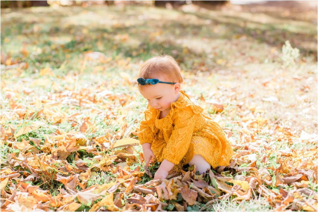 toddler in mustard colored dress playing with leaves