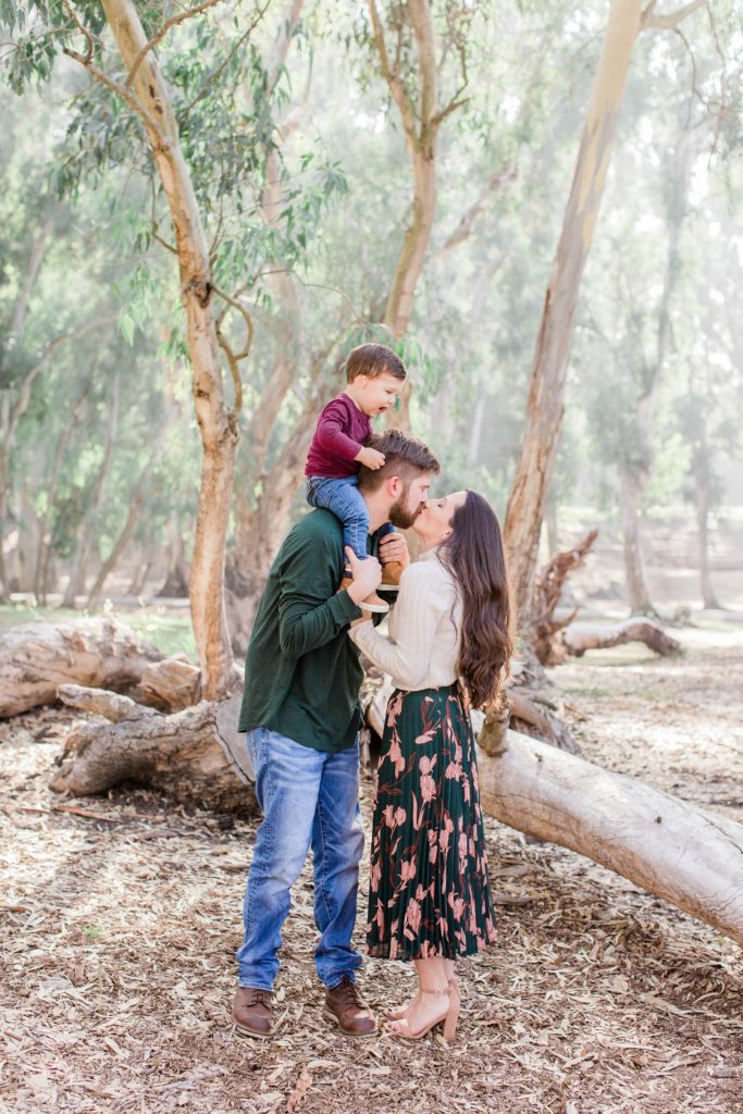 Mom and dad kissing with little boy on dad's shoulders