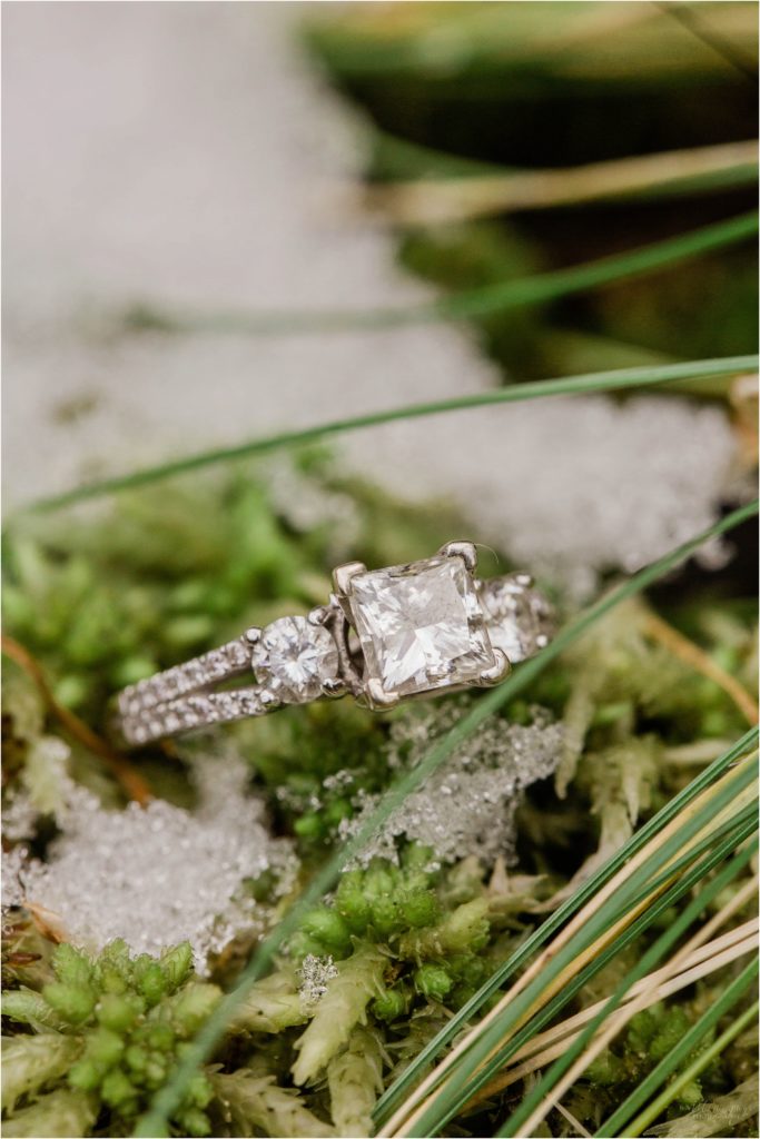Square cut engagement ring resting on pine needles in snow