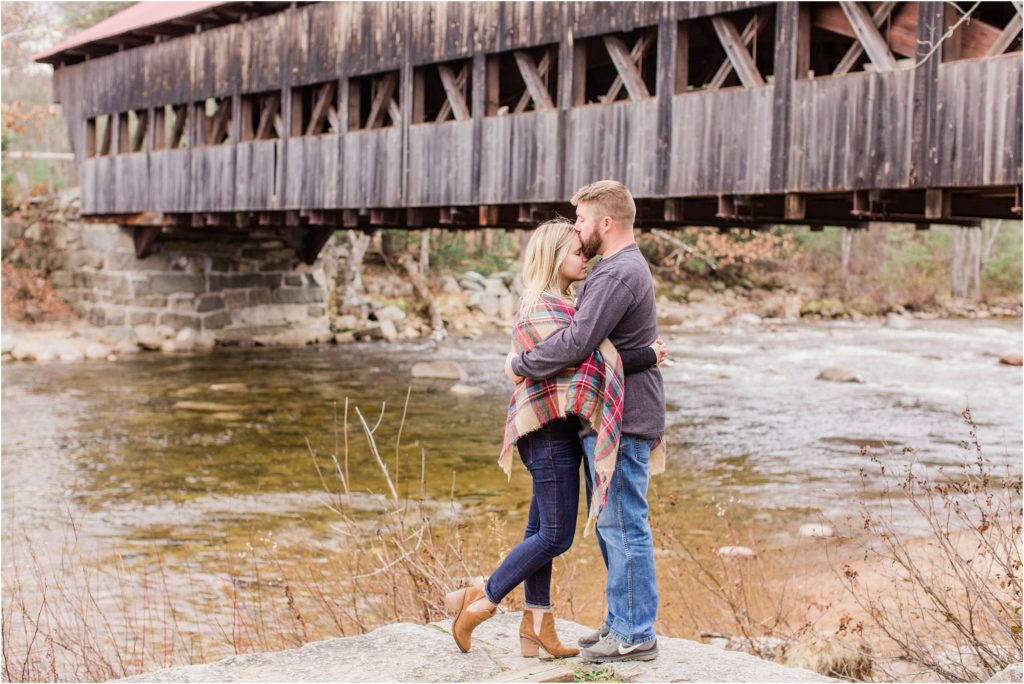 Man and woman snuggled together by covered bridge