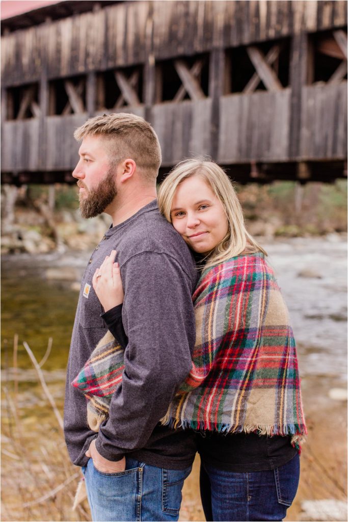 Man and woman snuggled together by covered bridge
