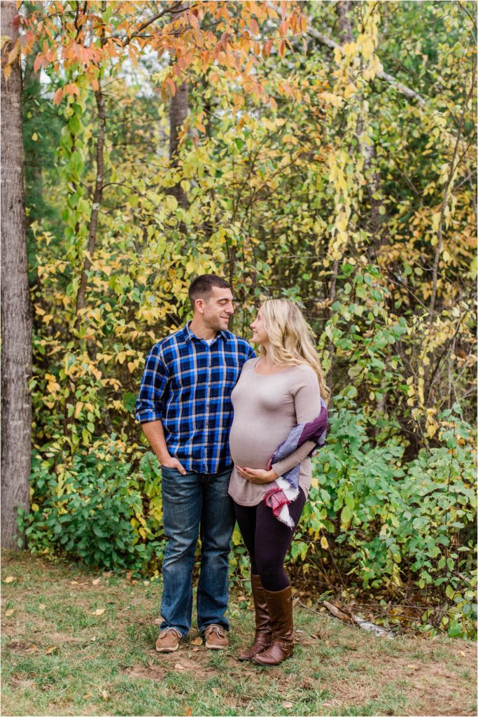 man and pregnant woman standing in front of autumn trees