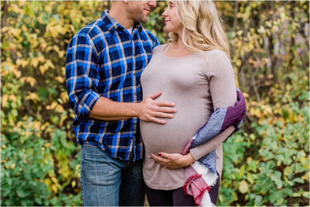 man and pregnant woman standing in front of autumn leaves