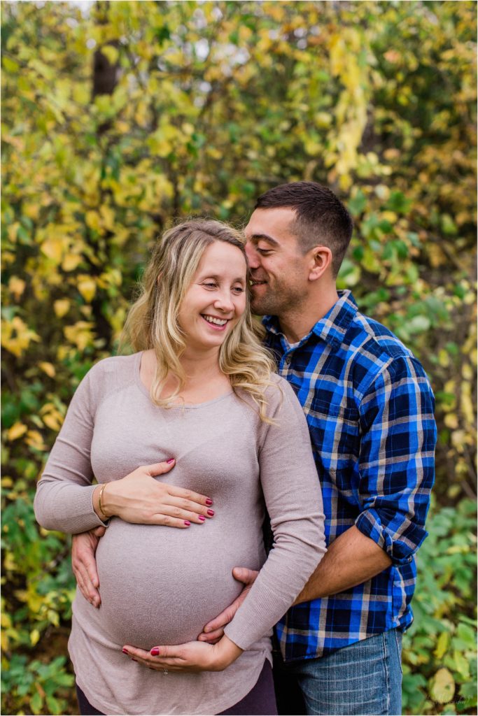 man and pregnant woman standing in front of autumn leaves