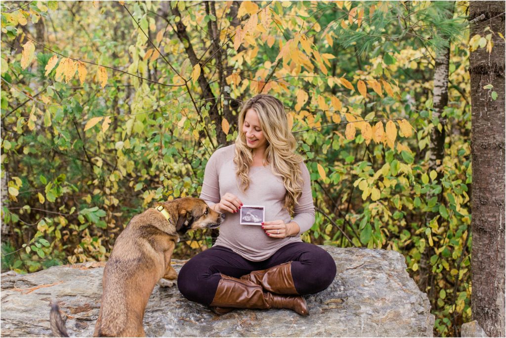 pregnant woman sitting rock holding ultrasound while dog looks on