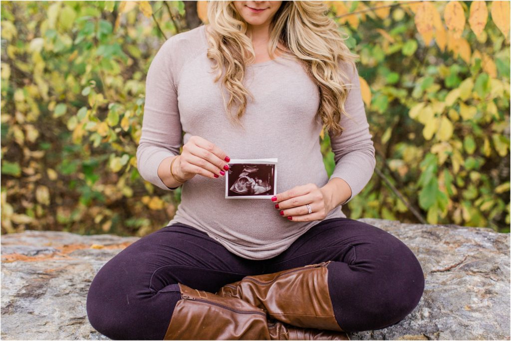 pregnant woman sitting on rock holding ultrasound photo