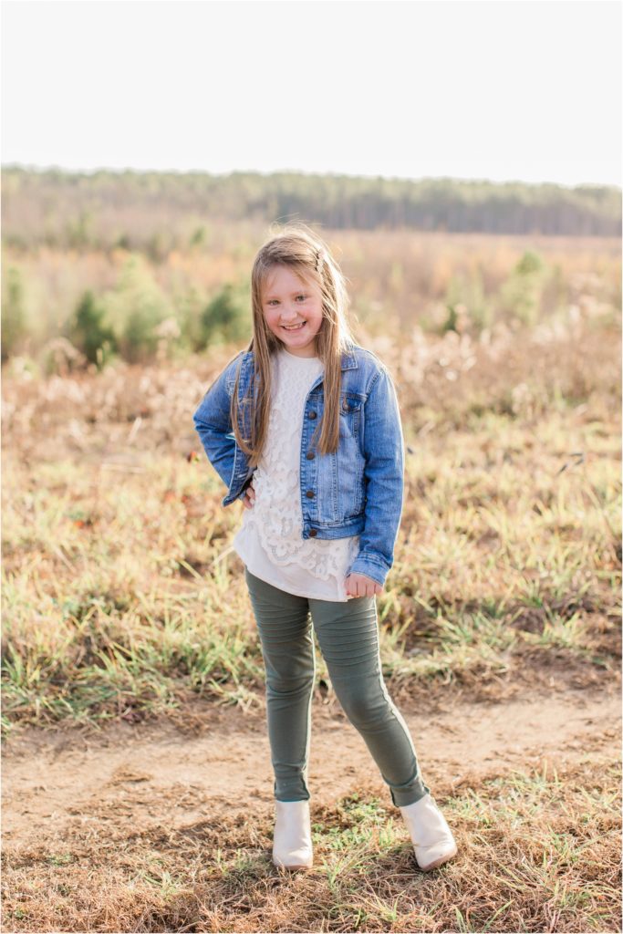 Girl in jean jacket standing in field with hand on her hip