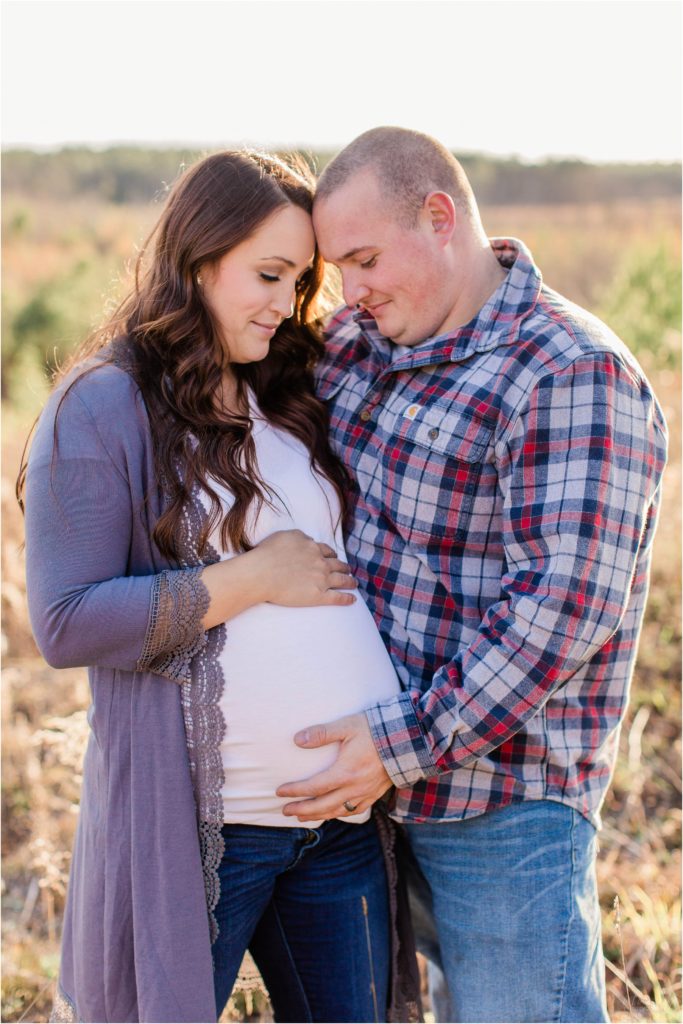 Man and pregnant wife standing together holding belly