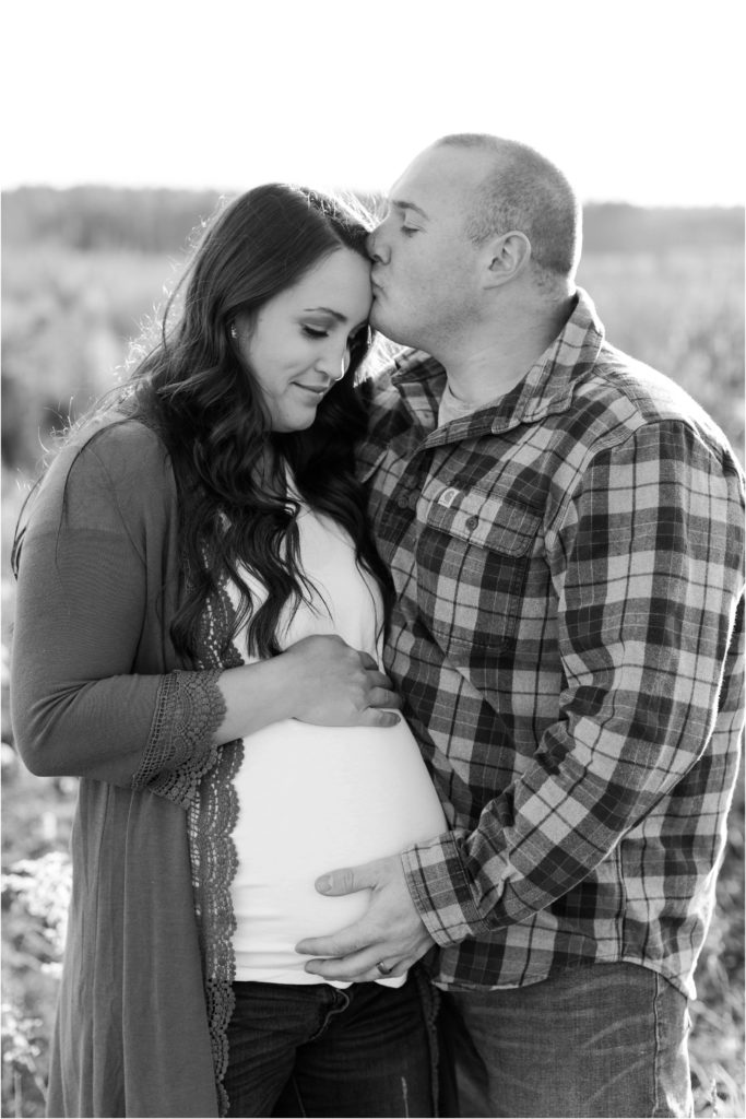 Black and white portrait of man and pregnant wife standing tougher holding onto the belly