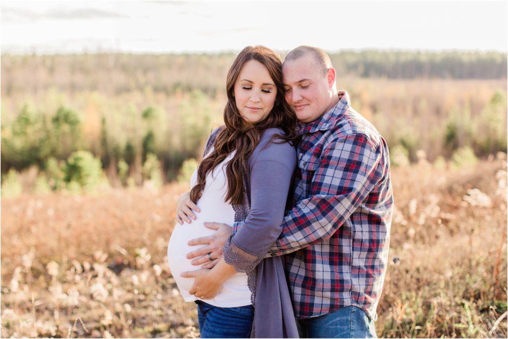 Man and pregnant wife standing together holding belly