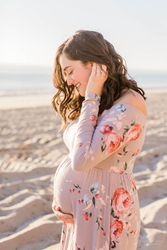 Pregnant woman holding her belly on the beach at sunset
