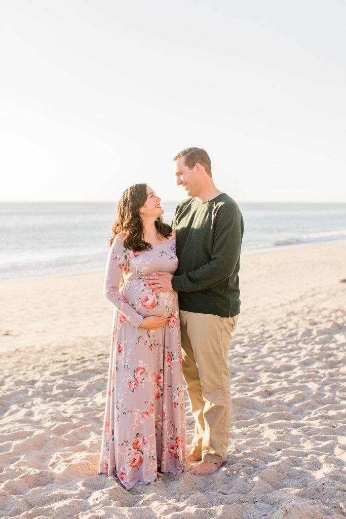 Couple standing together on the beach at sunset holding baby belly