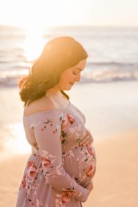 Pregnant woman holding her belly on the beach at sunset