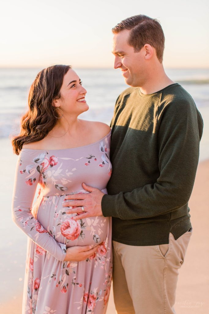 Couple holding baby belly on beach at sunset