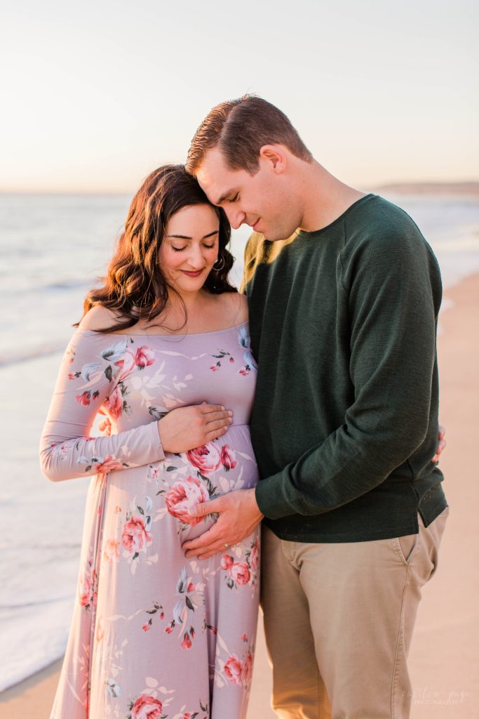 Couple holding baby belly on the beach at sunset