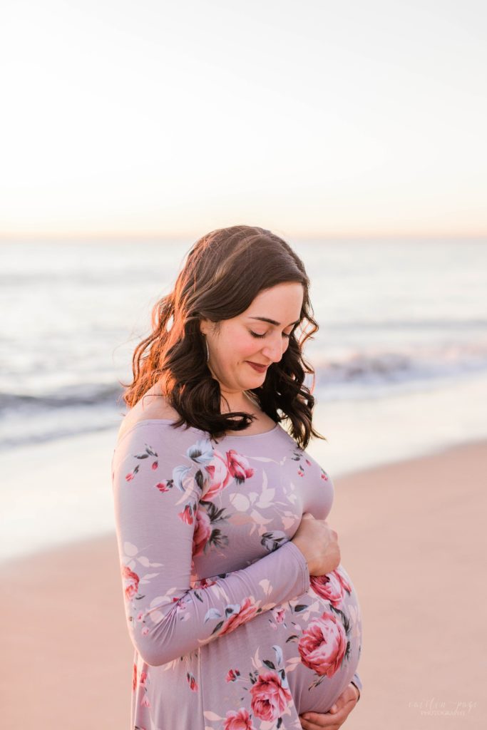 Pregnant woman holding her belly on the beach at sunset
