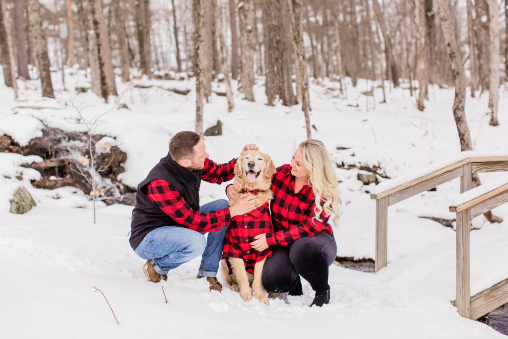 Couple in checkered shirts kneeling in the snow with golden retriever