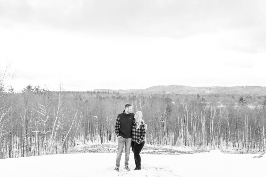 Black and white photo of couple standing on hill in snow