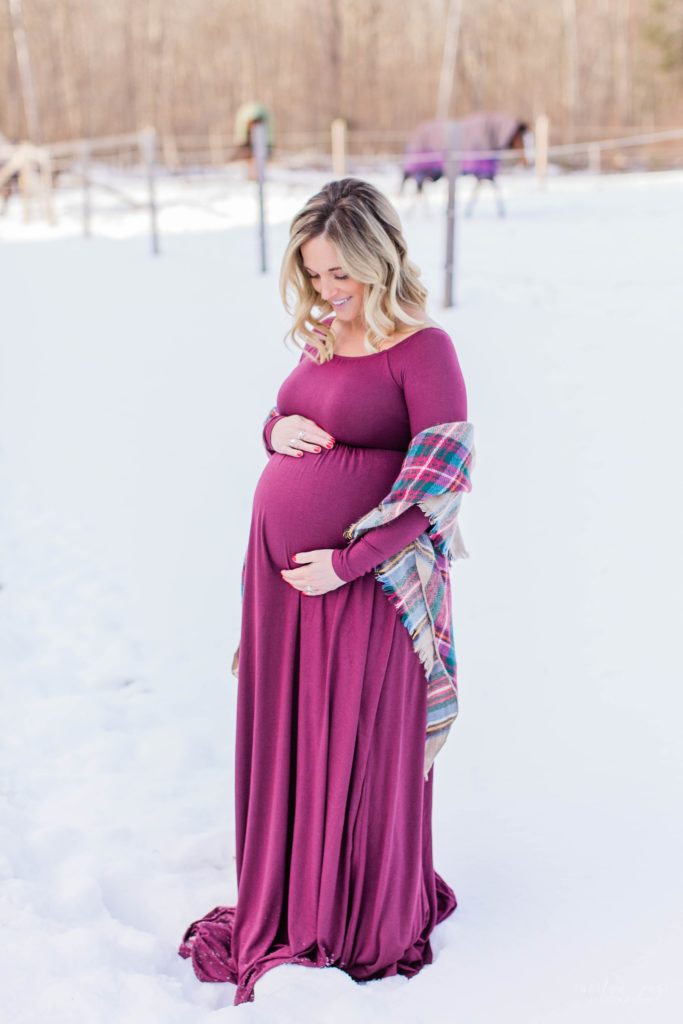 Pregnant woman standing in snow in burgundy dress