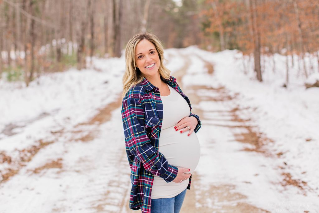 Pregnant woman in white shirt and checkered flannel shirt standing in road
