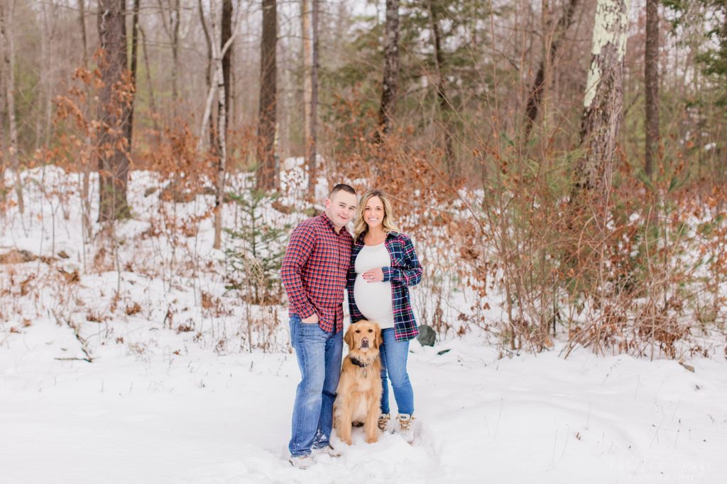 Man pregnant woman and dog standing together in the snow