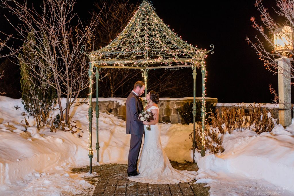 Bride and groom standing under gazebo in the snow with Christmas lights