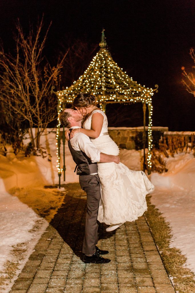 Groom holding bride in front of gazebo with Christmas lights