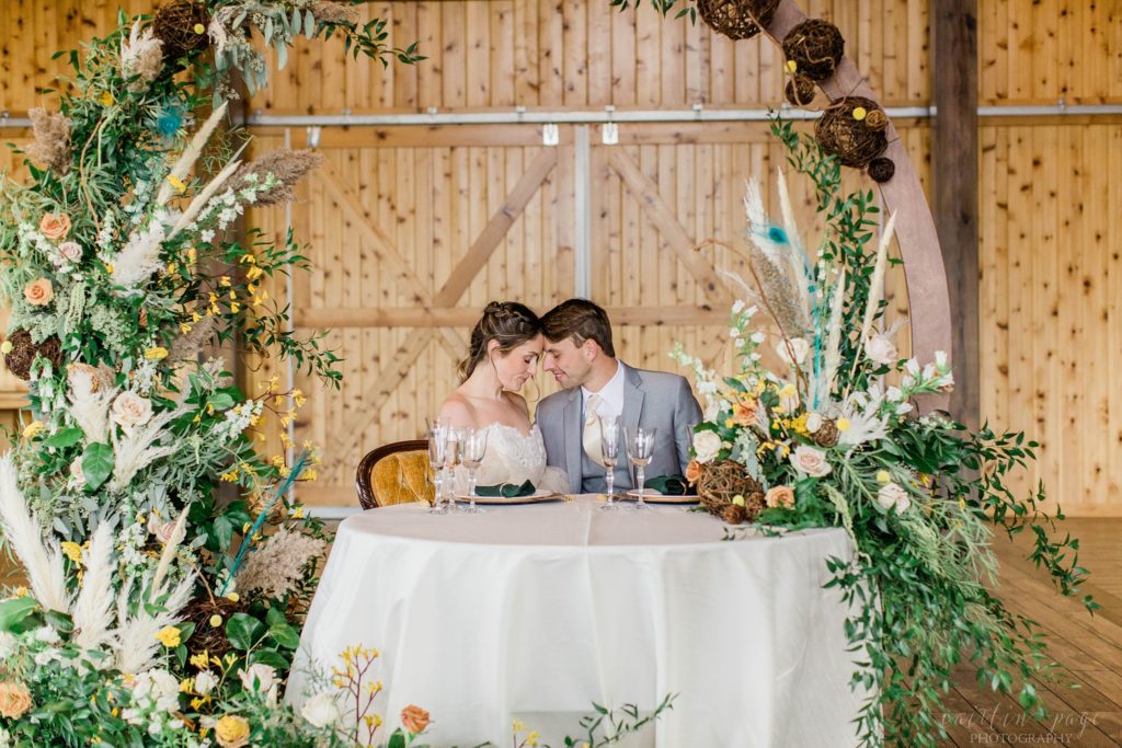 Couple sitting at head table with a hoop with floral display