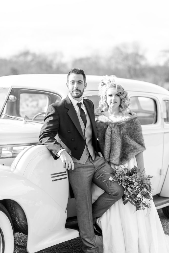 Black and white portrait of bride and groom standing in front of vintage car at Mount Ida Farm in Charlottesville Virginia