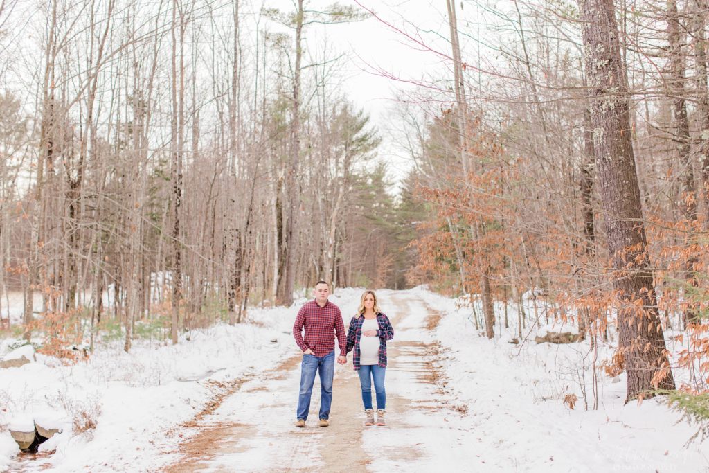 Man and pregnant woman standing in the middle of a dirt road with snow
