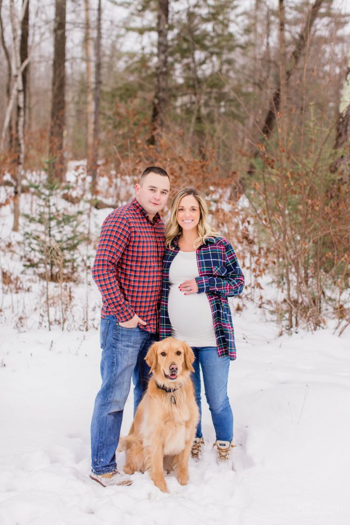 Man, pregnant woman and dog standing together in the snow