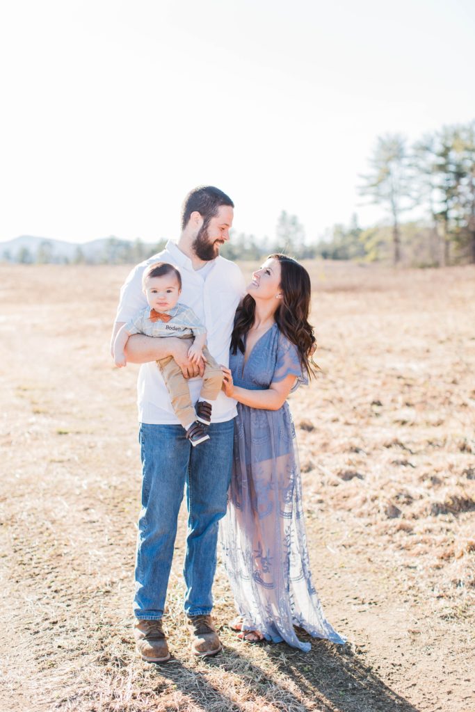 Man and woman looking at each other while dad holds baby boy in a field