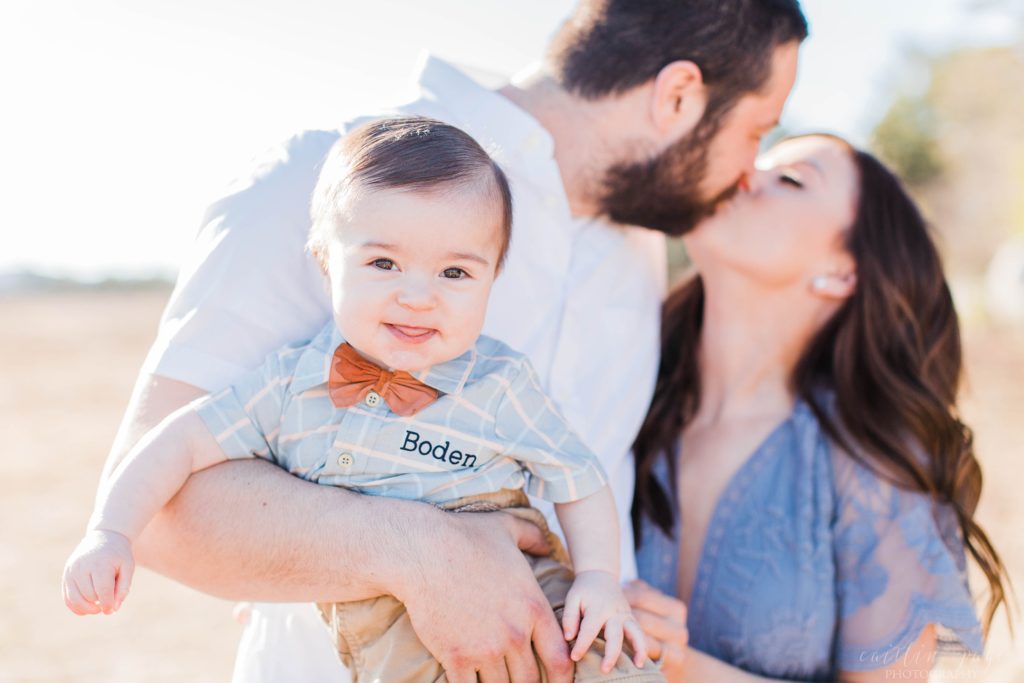 Man and woman kissing each other while baby boy smiles at camera