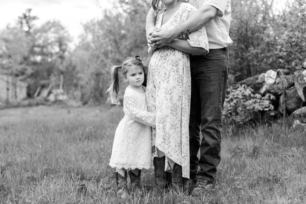 Black and white photo of little girl holding onto her moms leg in a field