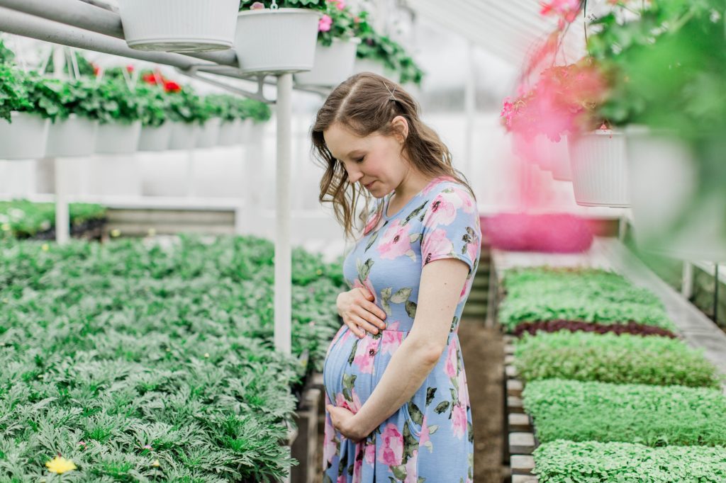 Woman holding onto her pregnant belly in a greenhouse