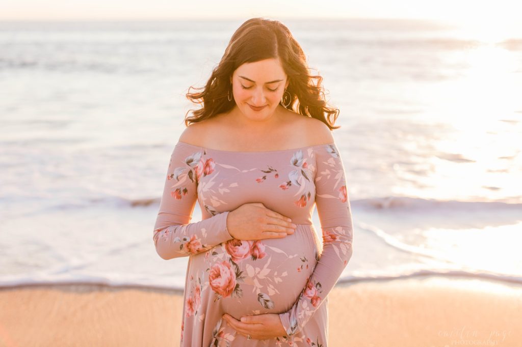 Pregnant woman holding onto her belly and looking at it at sunset on the beach in San Clemente California